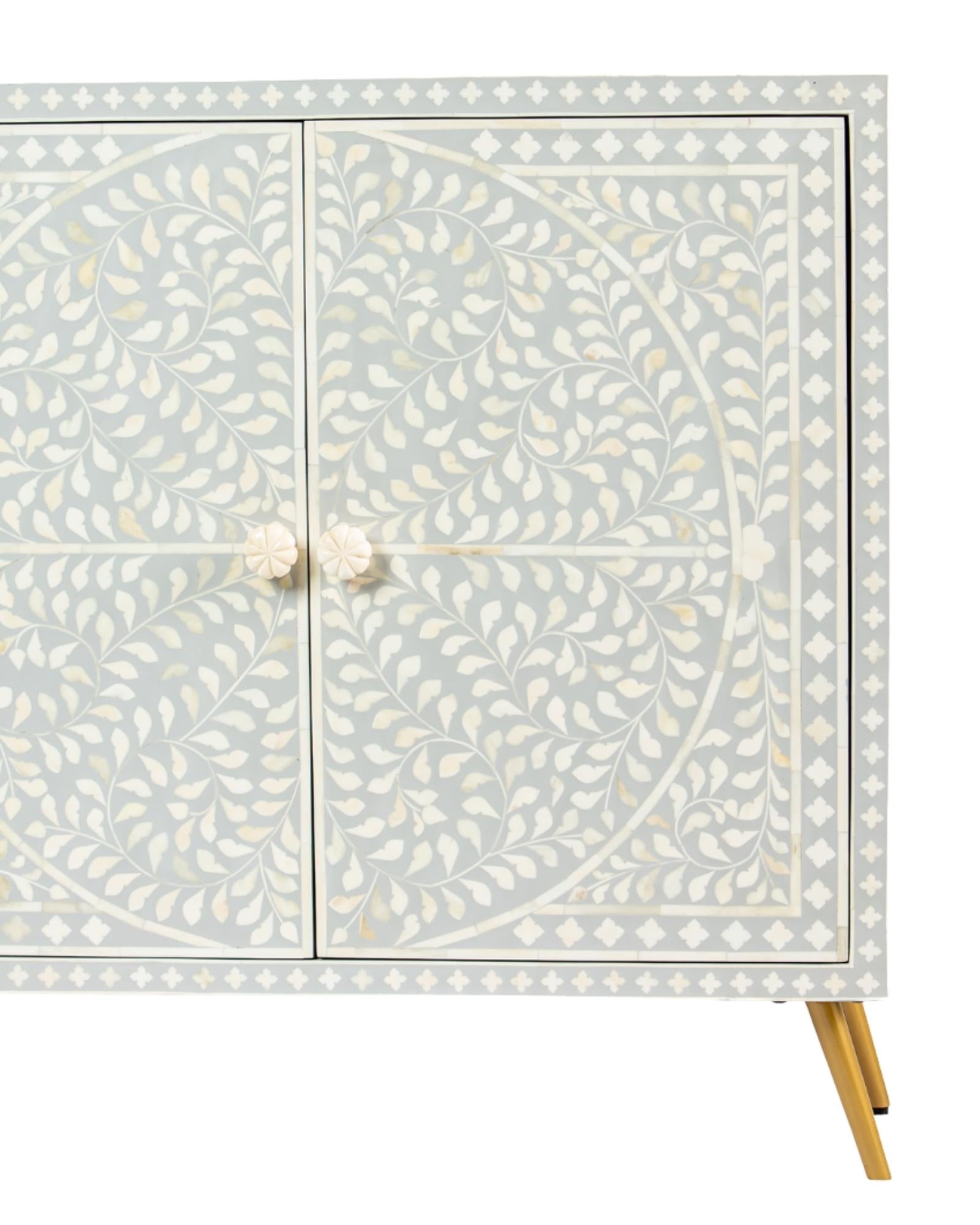 Grey bone inlay cabinet with floral vine pattern, brass legs, and carved bone knobs, handcrafted with spacious storage and artisanal charm.