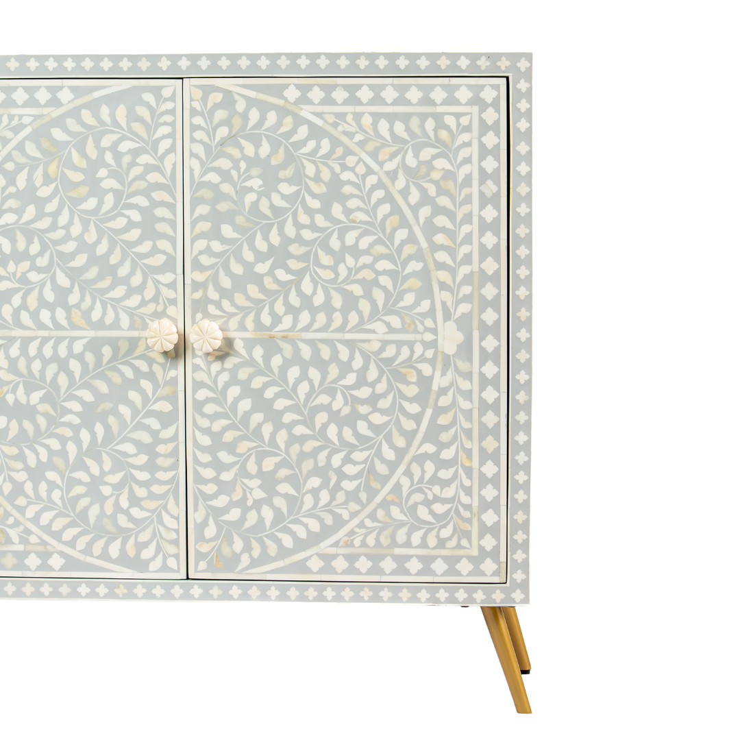 Grey bone inlay cabinet with floral vine pattern, brass legs, and carved bone knobs, handcrafted with spacious storage and artisanal charm.
