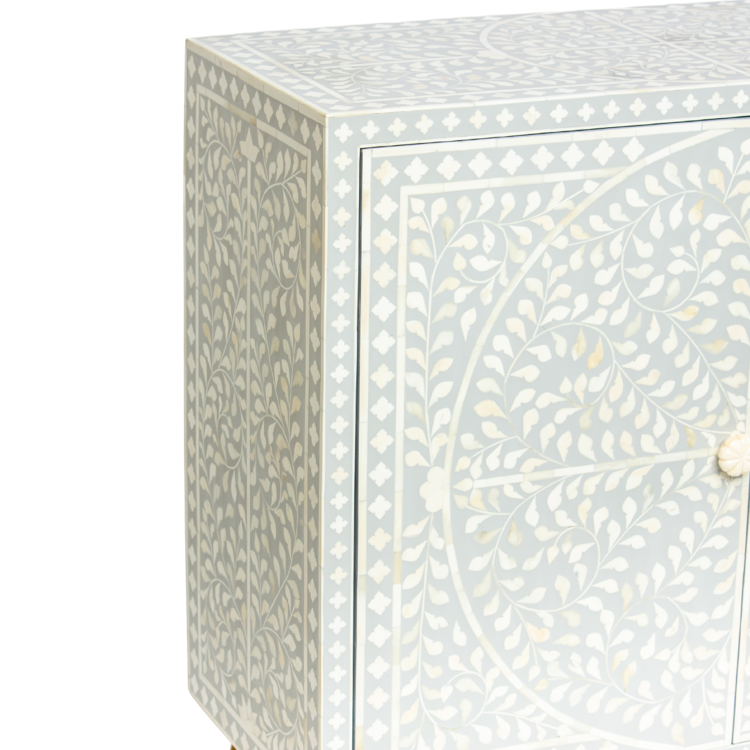 Grey bone inlay cabinet with floral vine pattern, brass legs, and carved bone knobs, handcrafted with spacious storage and artisanal charm.