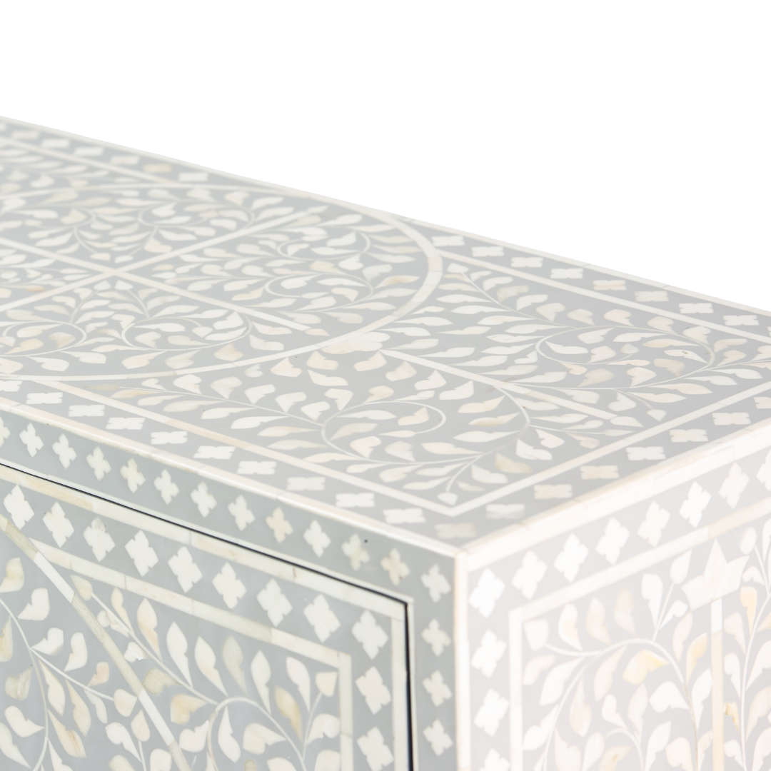 Grey bone inlay cabinet with floral vine pattern, brass legs, and carved bone knobs, handcrafted with spacious storage and artisanal charm.