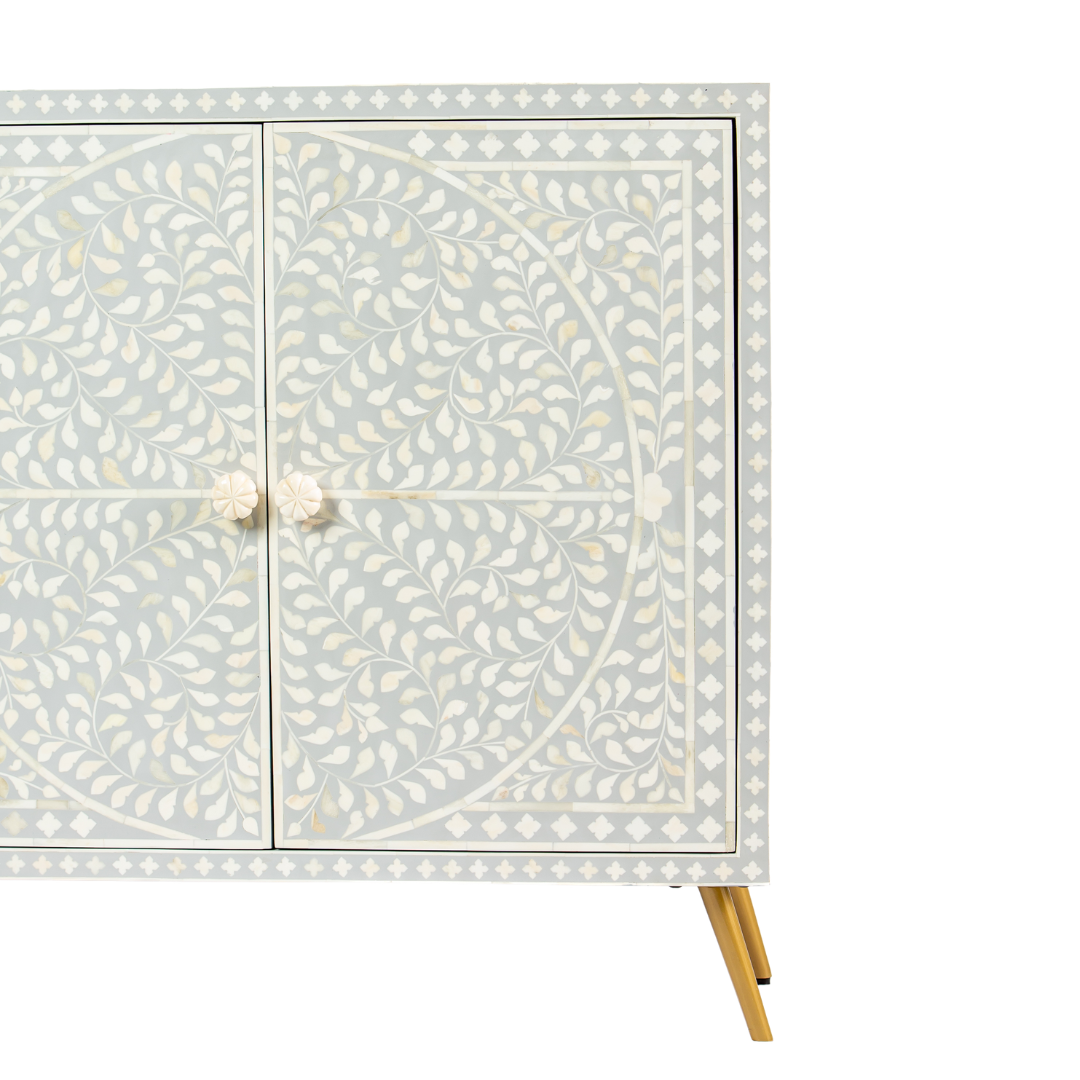 Grey bone inlay cabinet with floral vine pattern, brass legs, and carved bone knobs, handcrafted with spacious storage and artisanal charm.