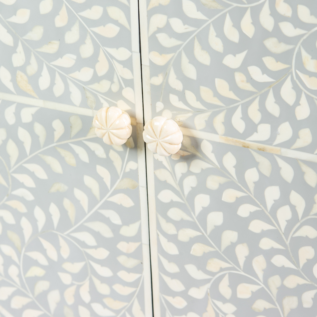 Grey bone inlay cabinet with floral vine pattern, brass legs, and carved bone knobs, handcrafted with spacious storage and artisanal charm.