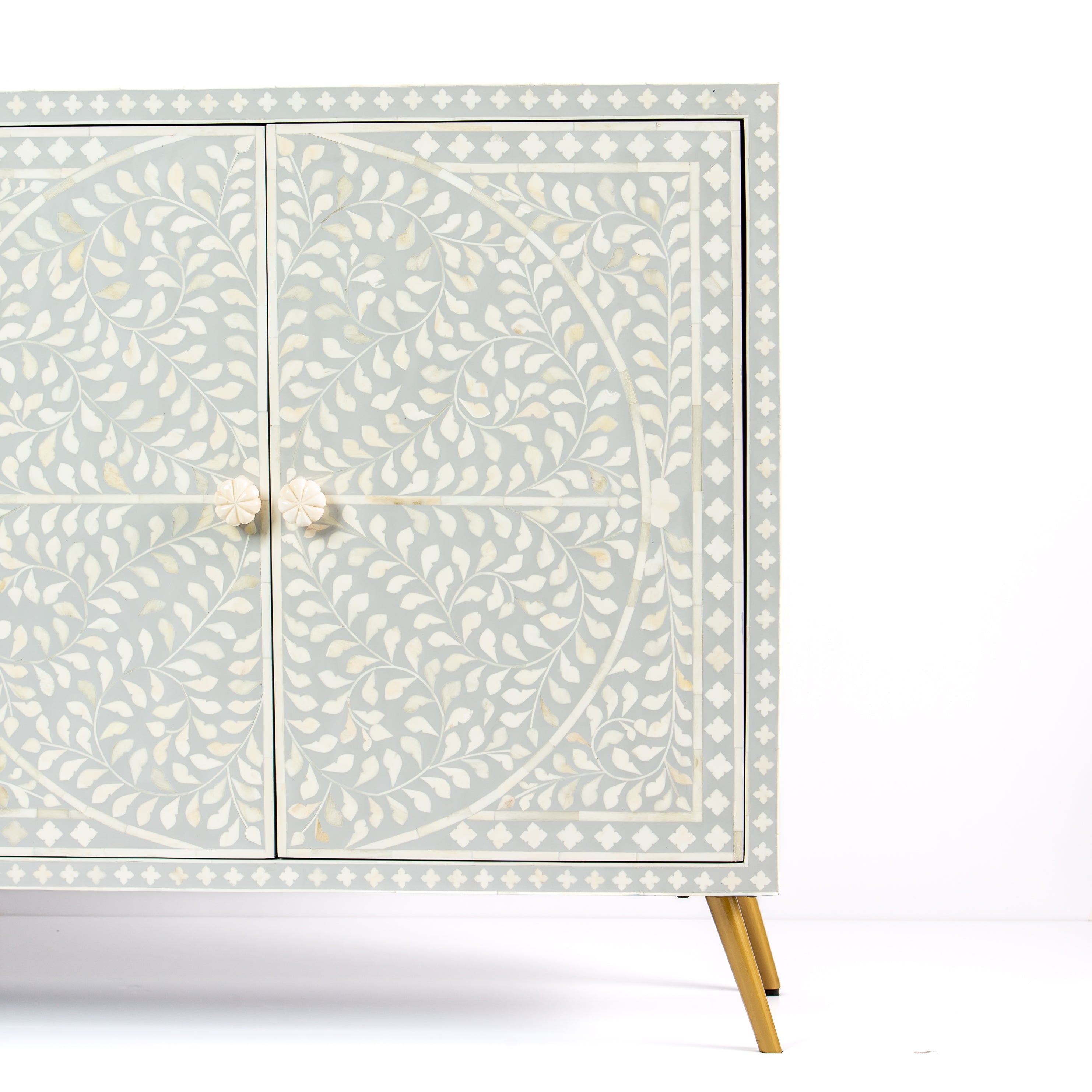 Grey bone inlay cabinet with floral vine pattern, brass legs, and carved bone knobs, handcrafted with spacious storage and artisanal charm.
