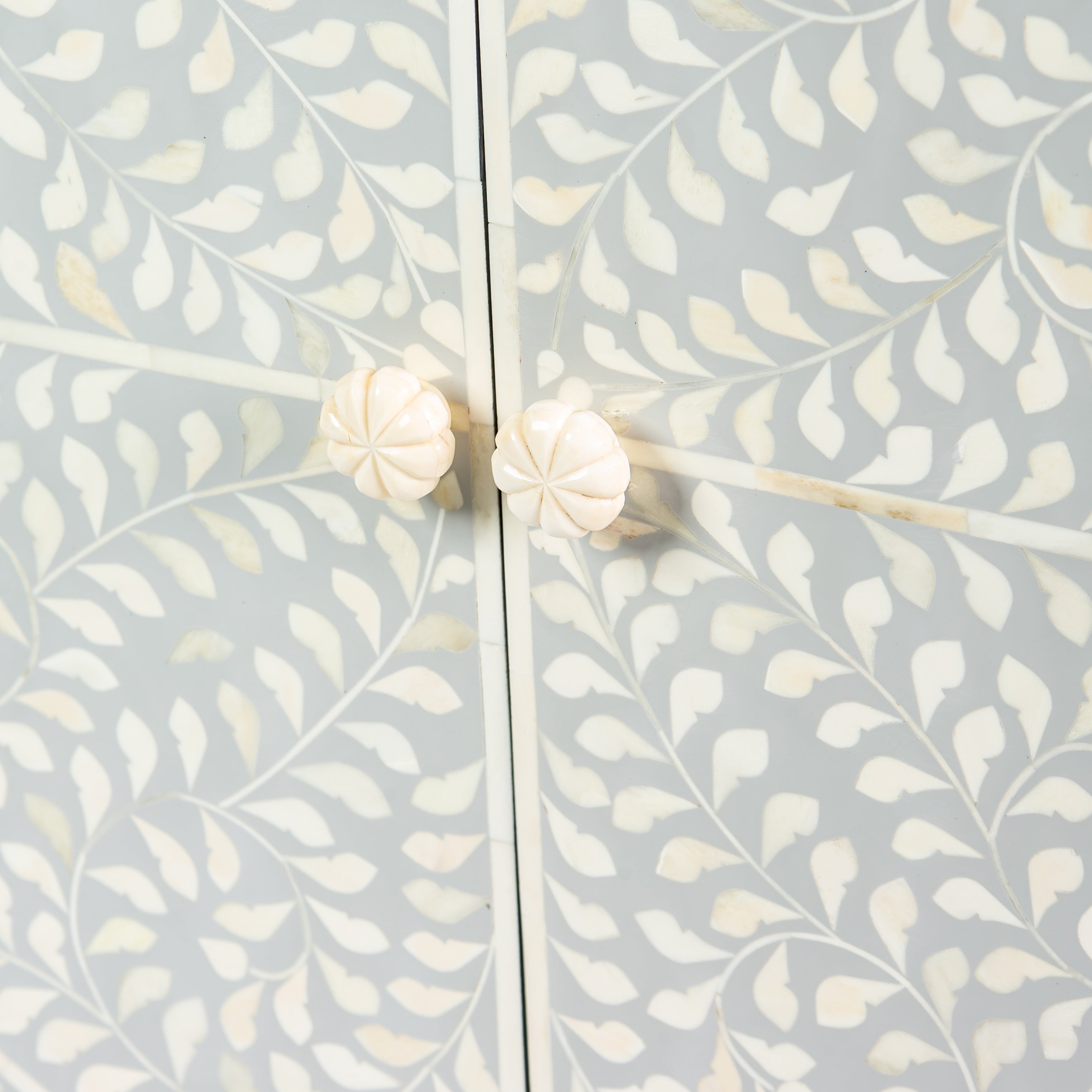 Grey bone inlay cabinet with floral vine pattern, brass legs, and carved bone knobs, handcrafted with spacious storage and artisanal charm.