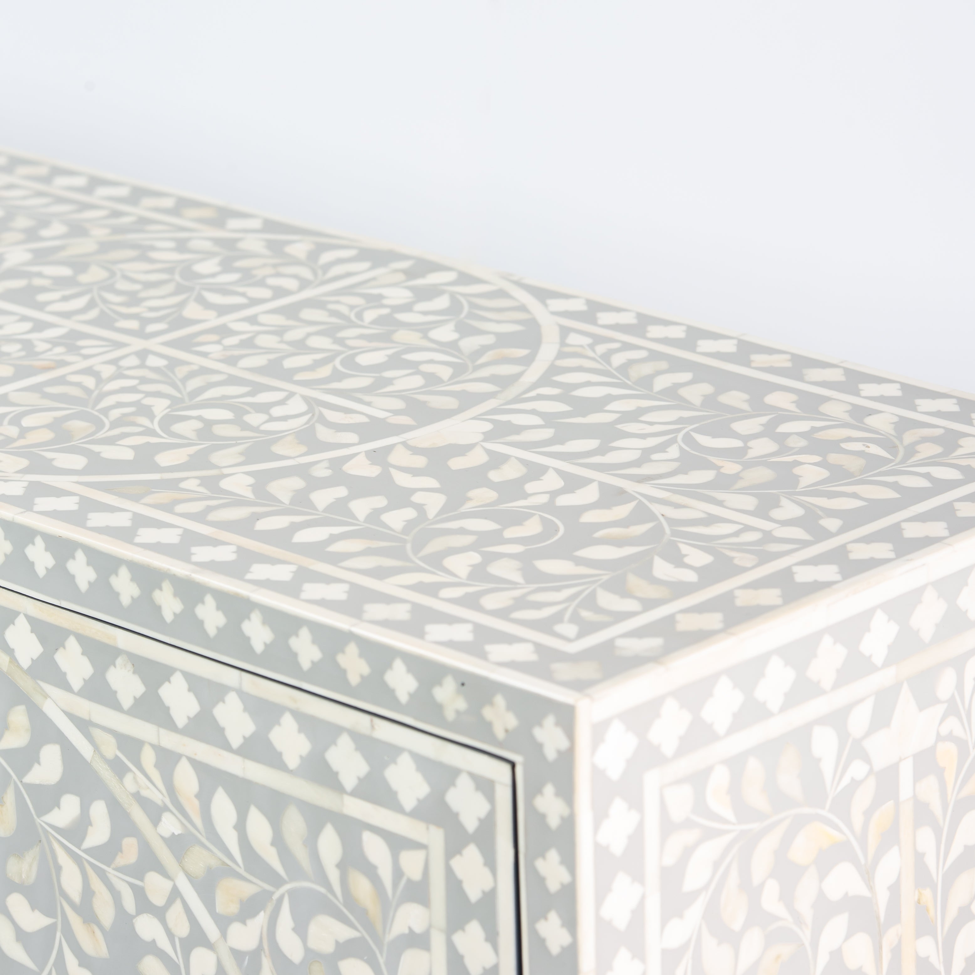 Grey bone inlay cabinet with floral vine pattern, brass legs, and carved bone knobs, handcrafted with spacious storage and artisanal charm.