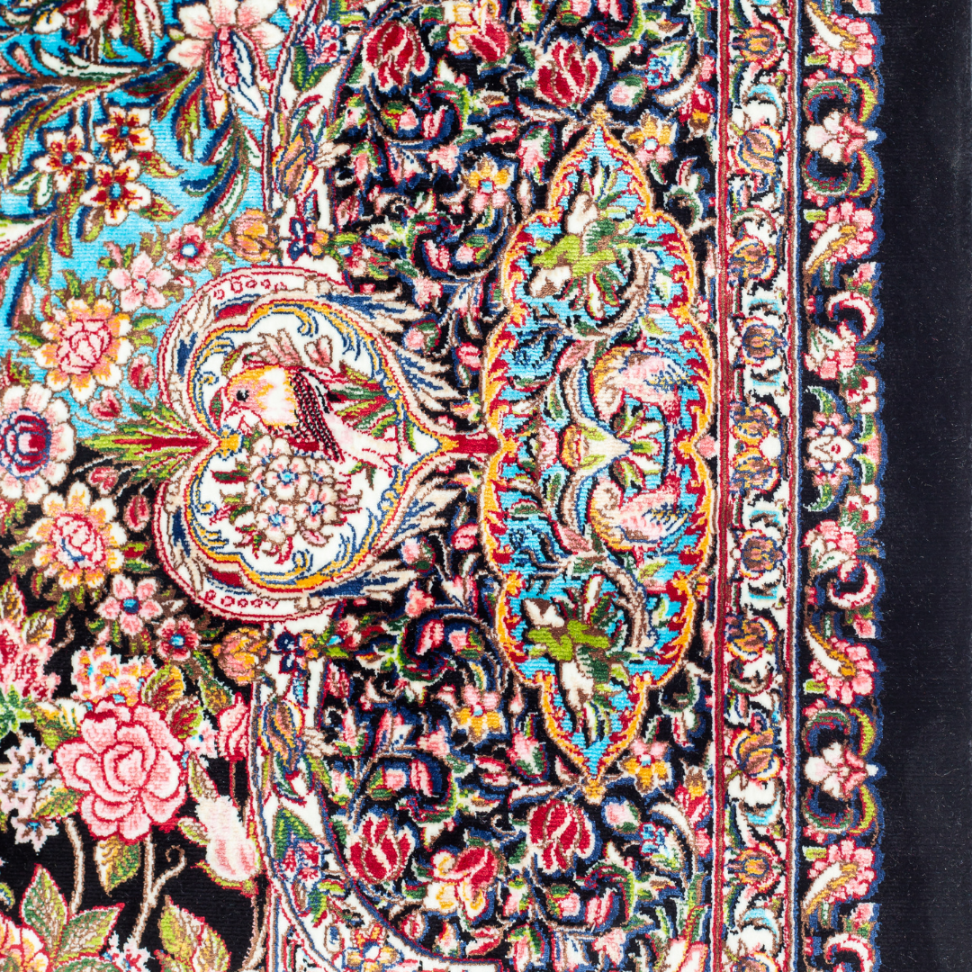 Close-up of the Sevi Persian silk rug featuring a floral and bird pattern in navy, turquoise, and gold tones. 150x100 cm size.