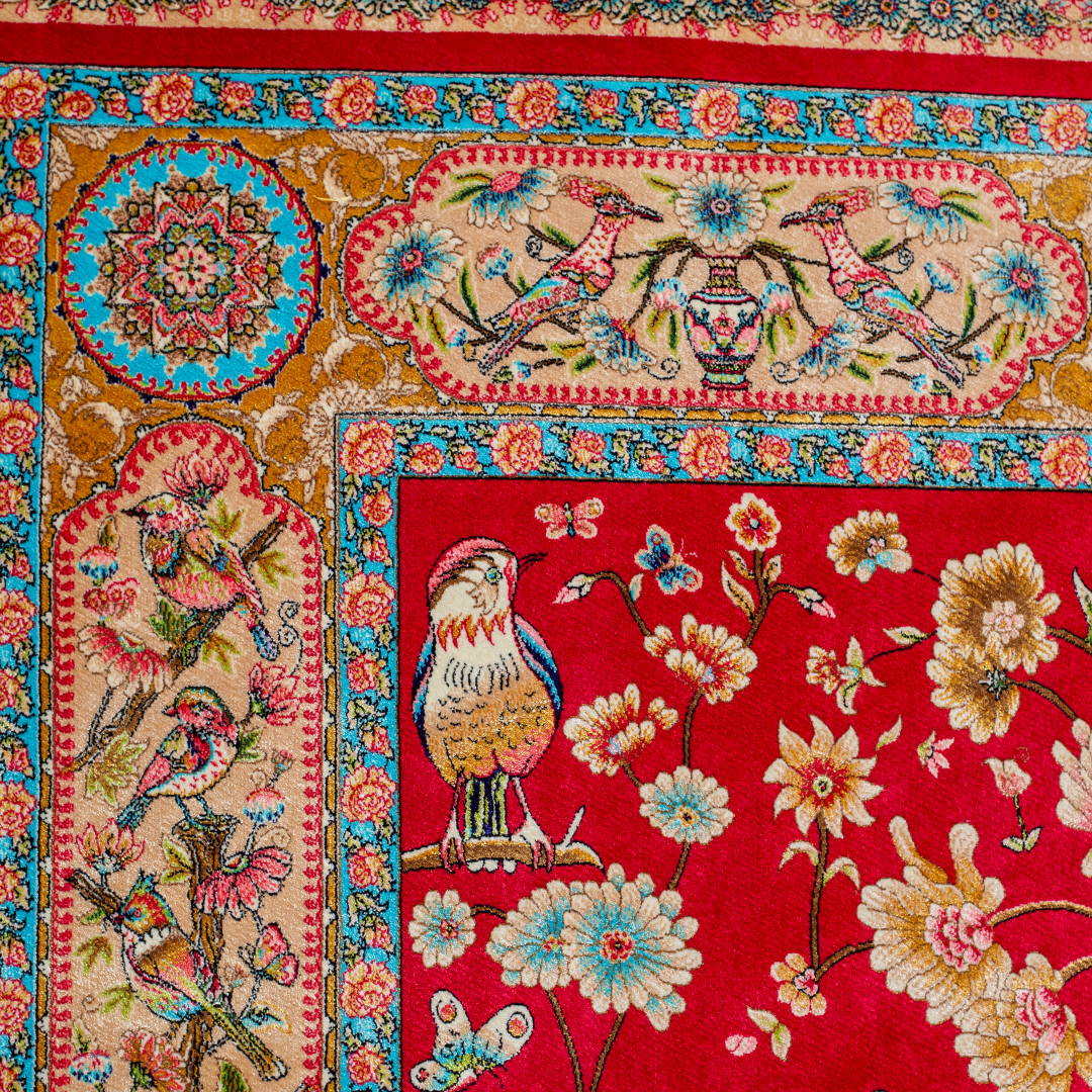 Crimson red silk rug featuring multi-colour floral and bird motifs, accented with turquoise, ivory, and gold detailing.