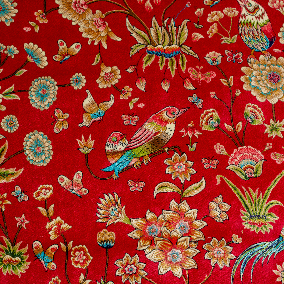 Crimson red silk rug featuring multi-colour floral and bird motifs, accented with turquoise, ivory, and gold detailing.