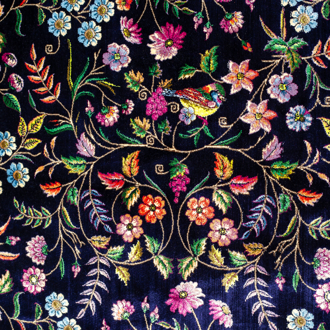 Navy silk rug with floral, bird, and vine motifs in pink, green, and multicolour tones, bordered in ivory.