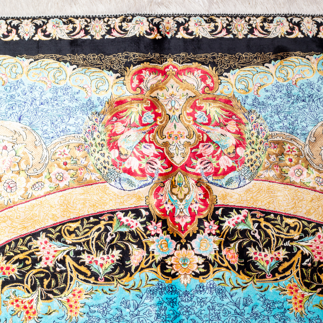 Luxury blue silk rug featuring a detailed central medallion, floral motifs, and ornate bird patterns in gold, coral, and black accents.