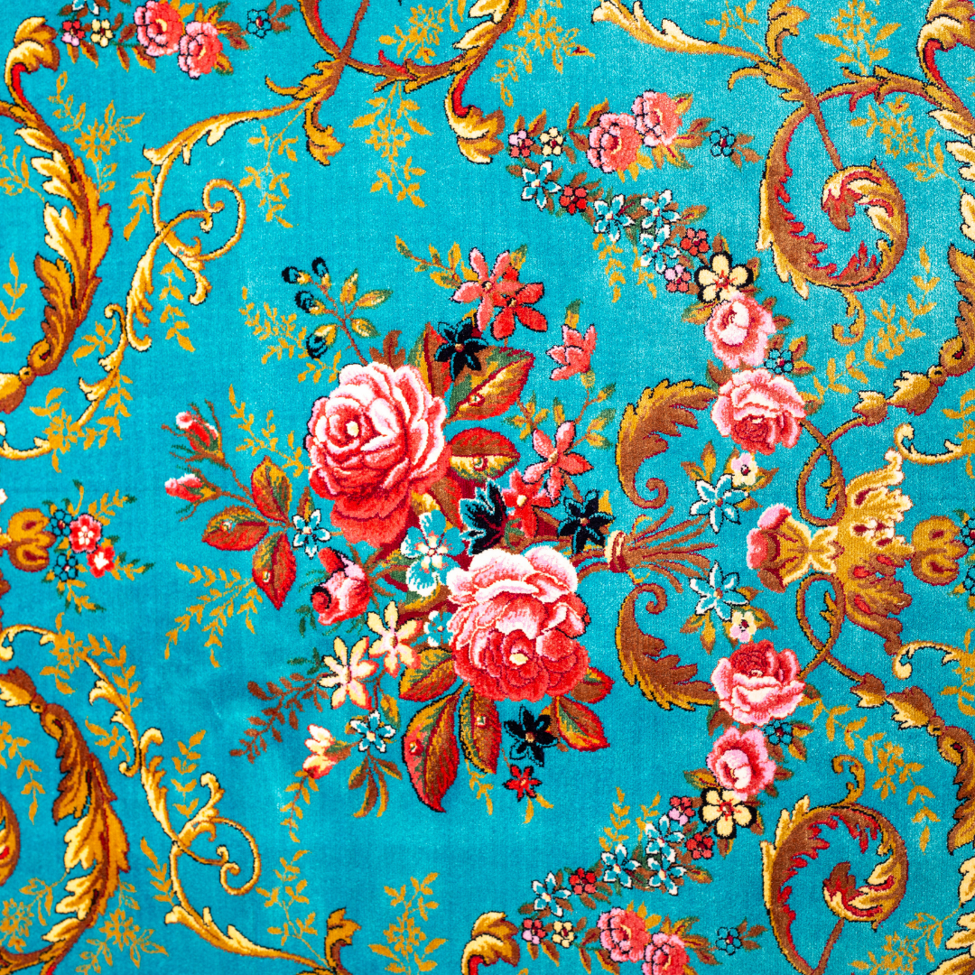 The Bellamy silk rug in turquoise with red floral motifs and golden scrolls, featuring a black ornamental border and exquisite handwoven detailing.