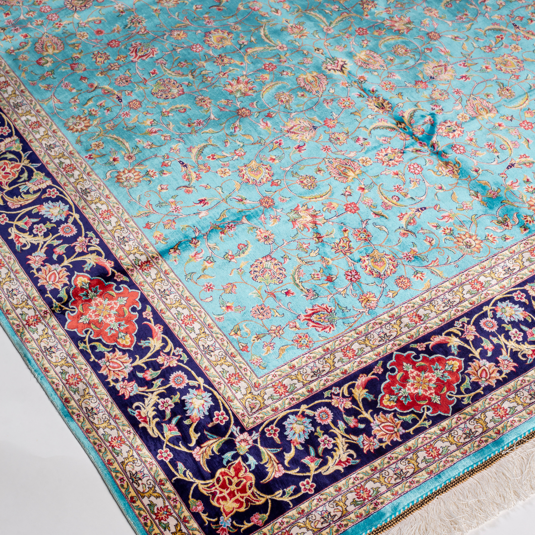 Aquamarine silk rug with coral and ivory floral motifs, framed by an indigo border. Handwoven with intricate detail and radiant sheen.