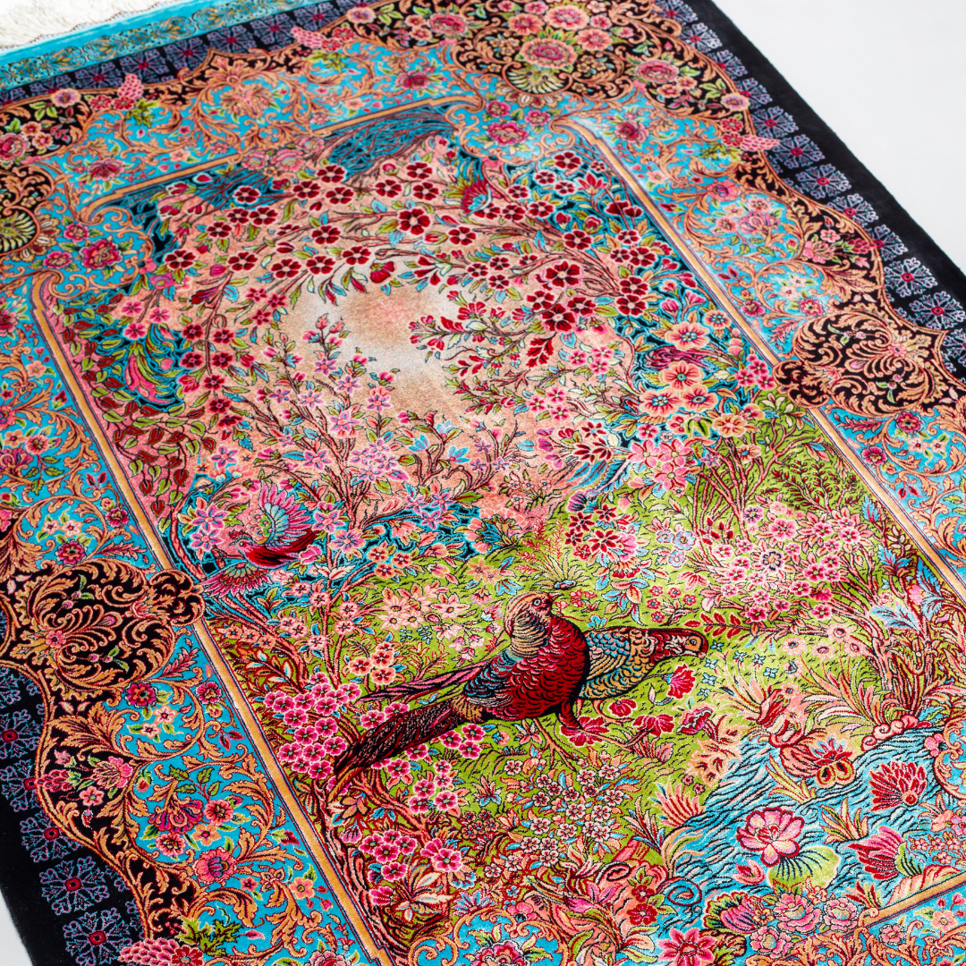 Elara Silk Rug featuring nature-inspired artwork with birds, flowers, and flowing water on an ivory base with turquoise and black borders, 150x100 cm.