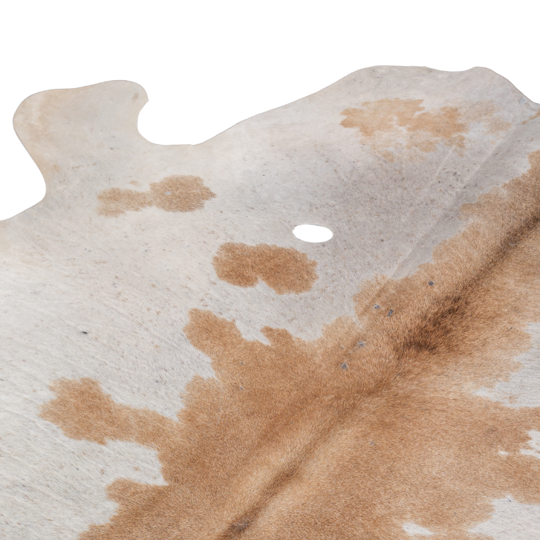 Natural cowhide rug with beige and chestnut brown markings, organic shape, and smooth textured finish.