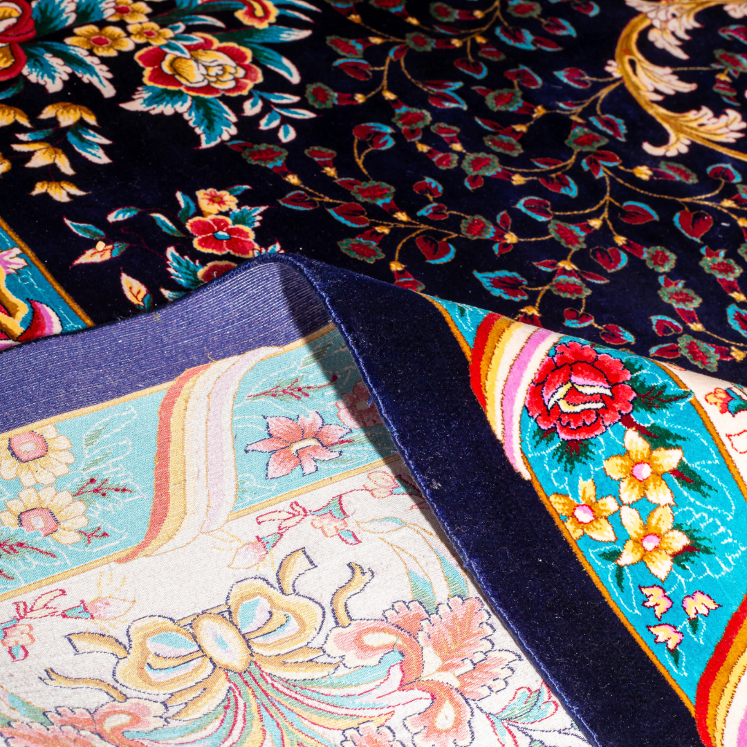 Elegant navy silk rug with detailed floral medallion, ornate cream border, and rich Persian-inspired design in gold, coral, and turquoise tones.