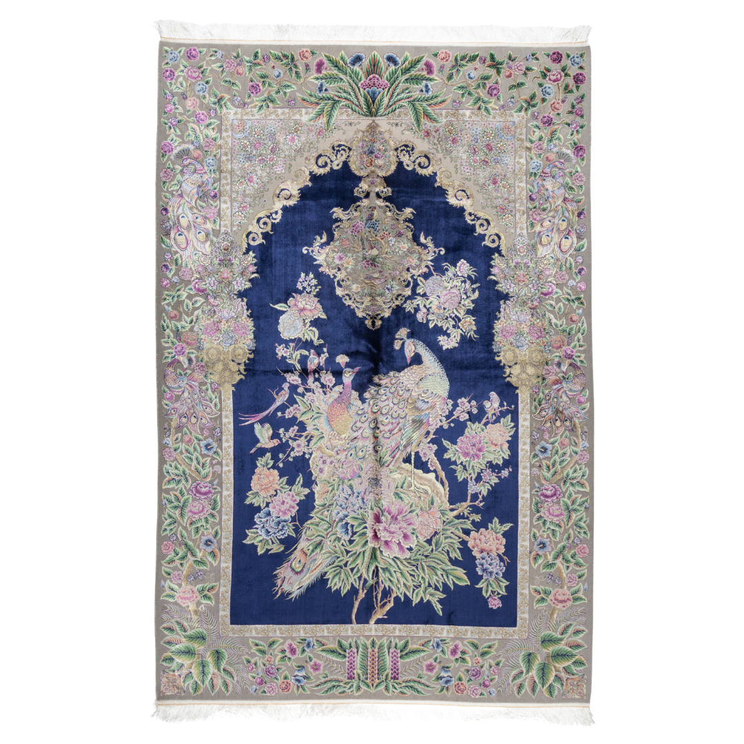 Luxurious silk rug with peacock pair and blooming florals on a navy base. Handwoven in soft hues with intricate botanical detailing.