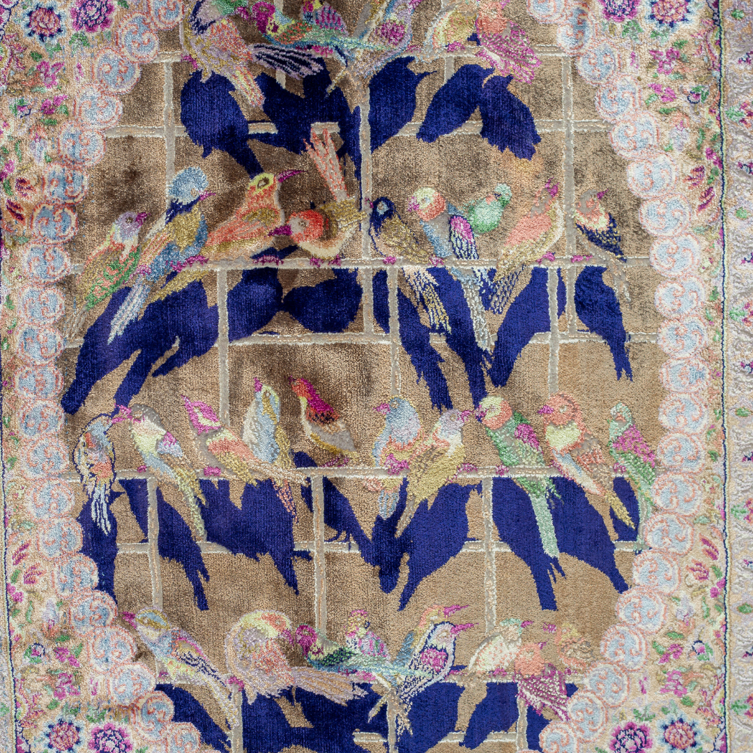 Luxurious silk rug with central bird tree, bordered by peacocks and florals. Handwoven in soft jewel tones with ornate framed details.