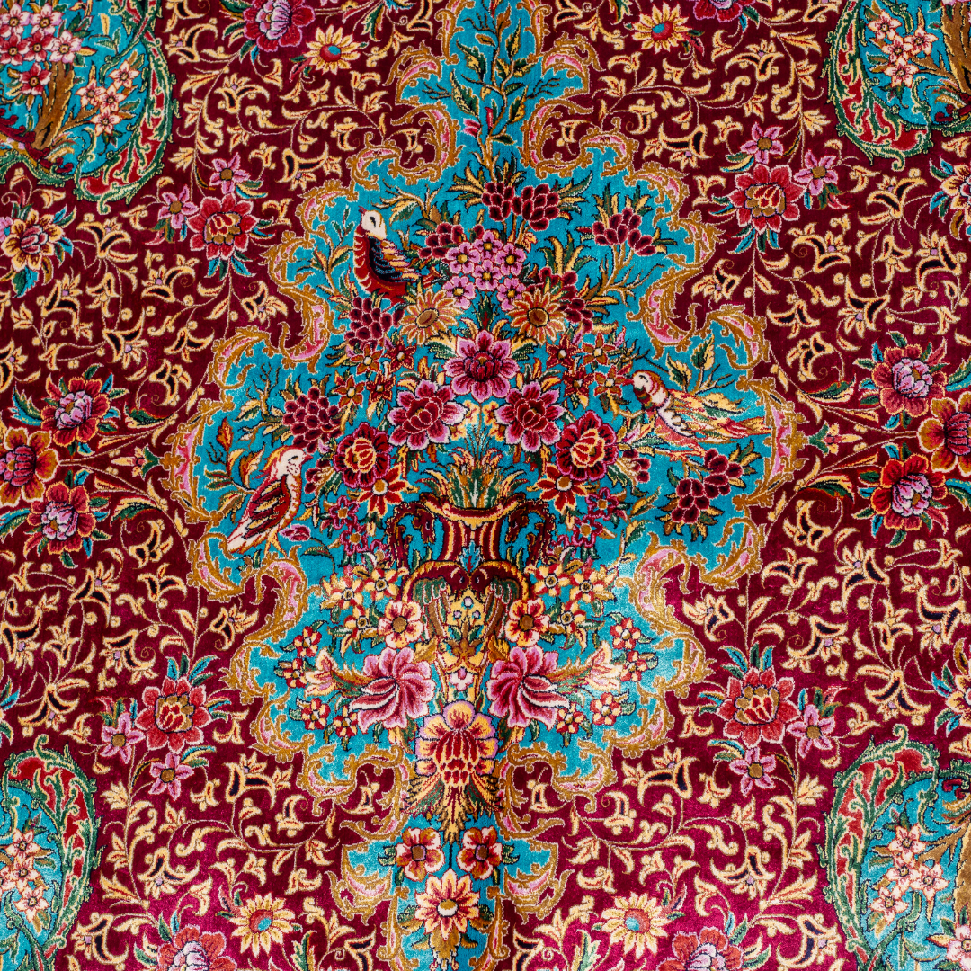 Opulent silk rug with ruby base and turquoise floral accents. Detailed handwoven artistry ideal for luxury, dramatic interior settings.