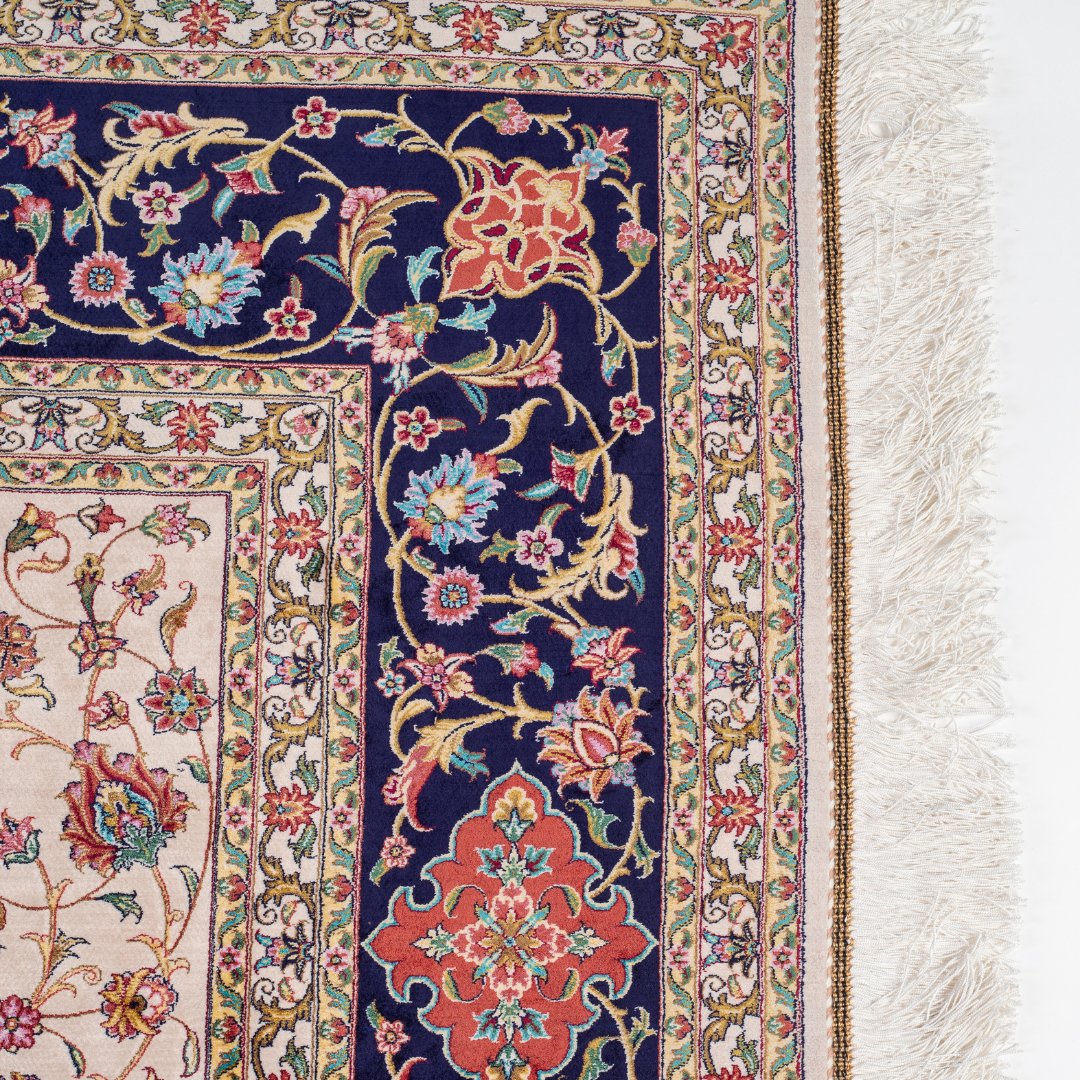 Ivory silk rug with intricate floral patterns in navy, rose, gold, and turquoise, framed with an ornate navy border.