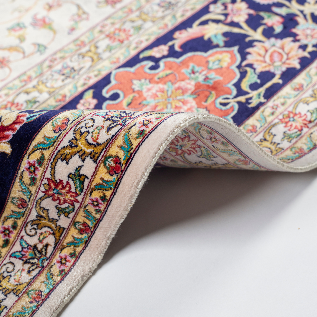 Ivory silk rug with intricate floral patterns in navy, rose, gold, and turquoise, framed with an ornate navy border.