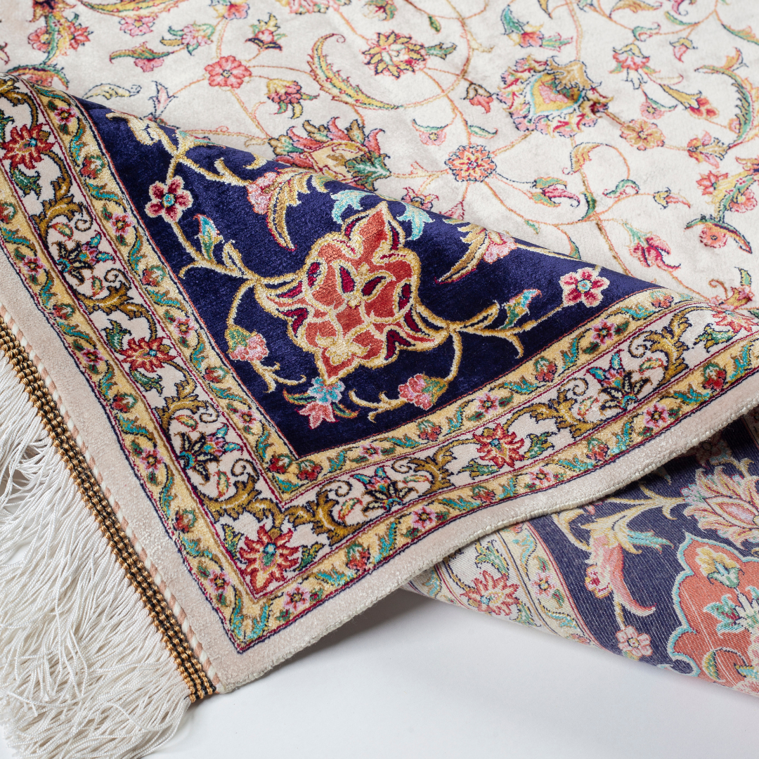 Ivory silk rug with intricate floral patterns in navy, rose, gold, and turquoise, framed with an ornate navy border.