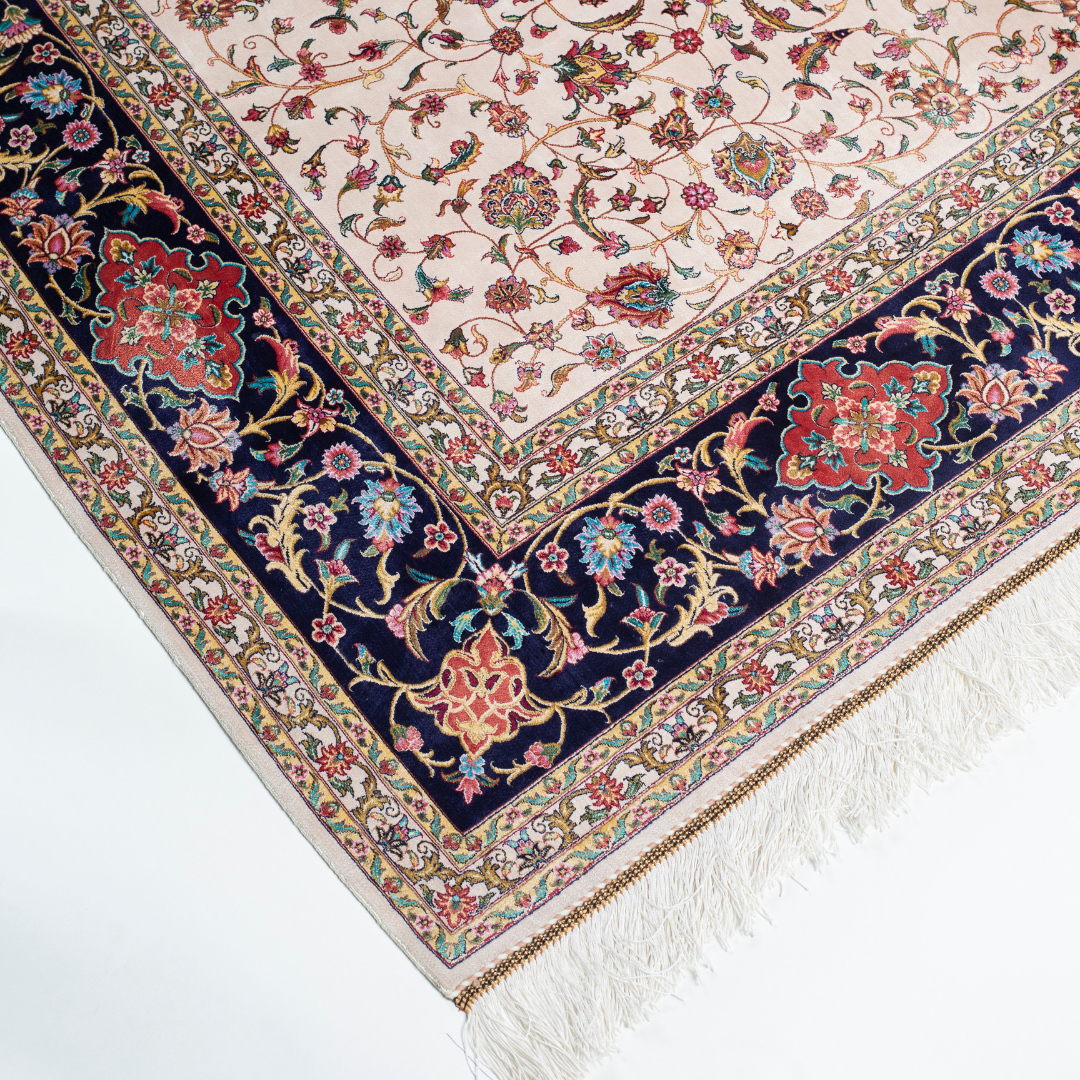 Ivory silk rug with intricate floral patterns in navy, rose, gold, and turquoise, framed with an ornate navy border.