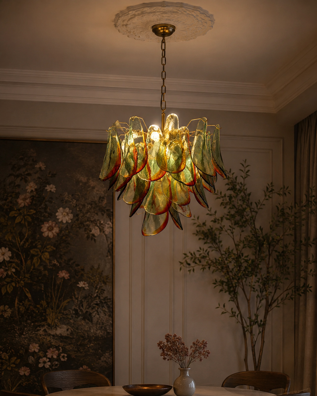 The Botanic Chandelier by The Qratist features handcrafted green and amber glass leaves layered around a refined metal frame, creating a sculptural botanical statement inspired by nature.