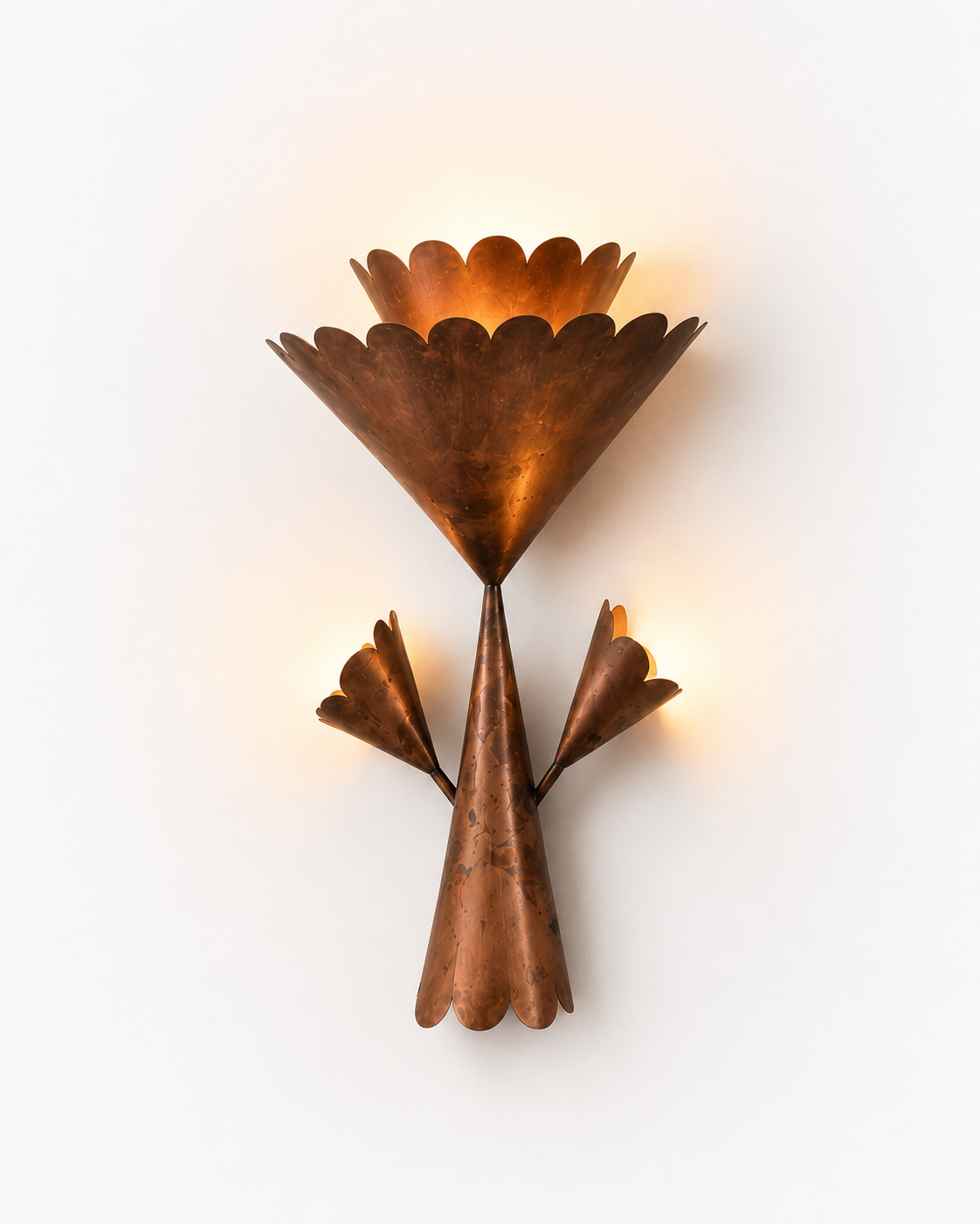 The Corsage Wall Light by The Qratist features handcrafted copper finished metal petals arranged in a sculptural floral composition that creates warm ambient illumination.