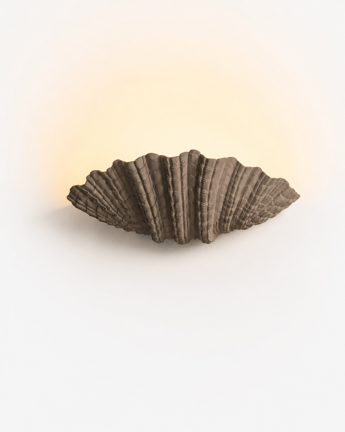 The Grotto Wall Light by The Qratist features a handcrafted sculptural form inspired by coastal grottos, crafted from plaster, polyresin, and sandstone to create warm ambient illumination.