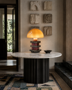 The Pagoda Lamp by The Qratist features a handcrafted amber blown glass dome balanced above sculptural glass columns and layered granite accents, creating a luxurious architectural statement table lamp.