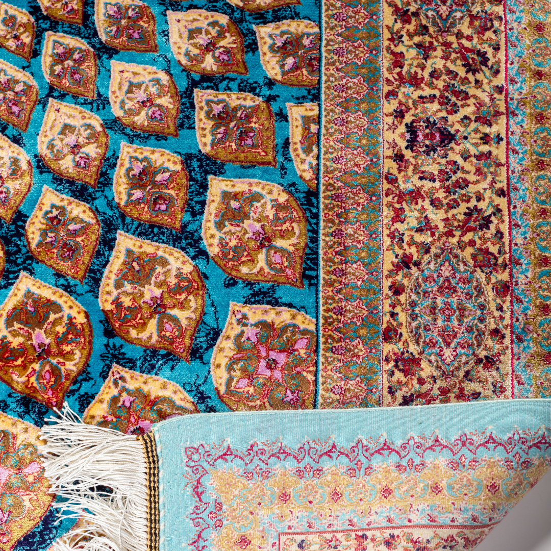 Verta silk rug featuring a turquoise blue base with intricate gold, ruby red, ivory, and fuchsia floral medallion design in a symmetrical pattern.