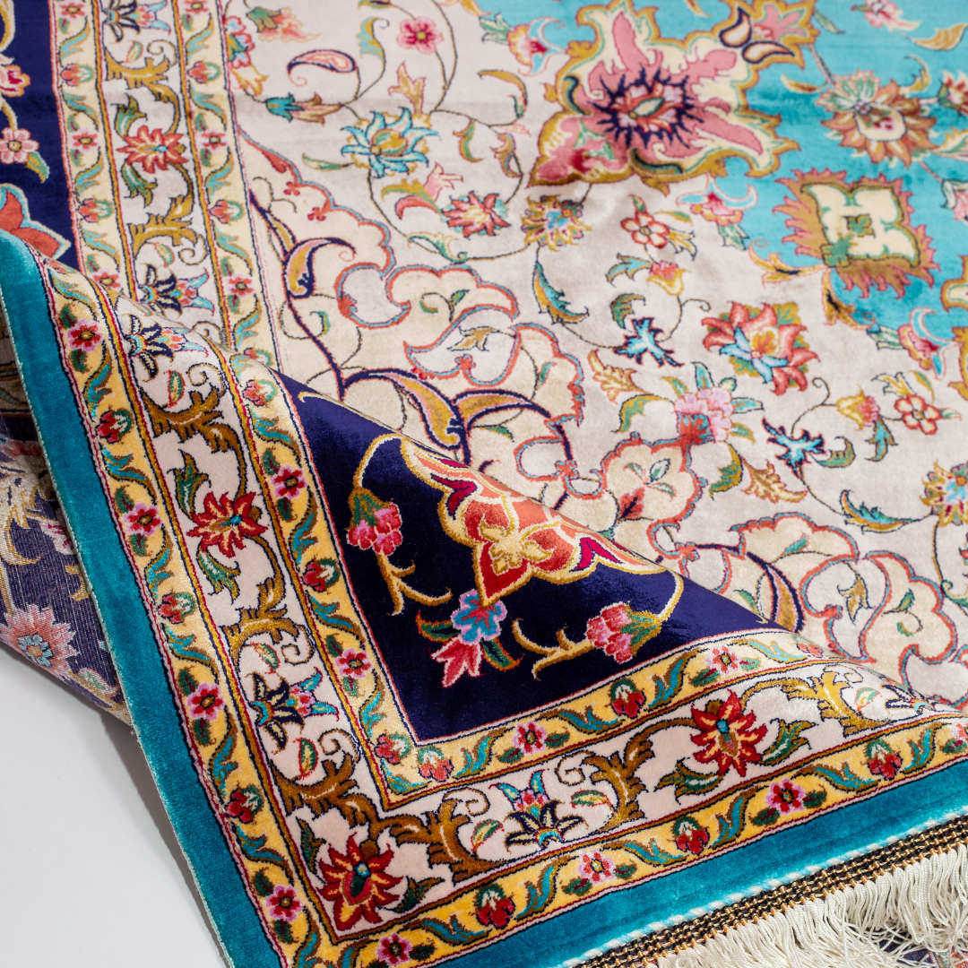 Intricately designed silk rug with turquoise base, floral patterns, and central medallion in red and gold – hand-finished and richly detailed.