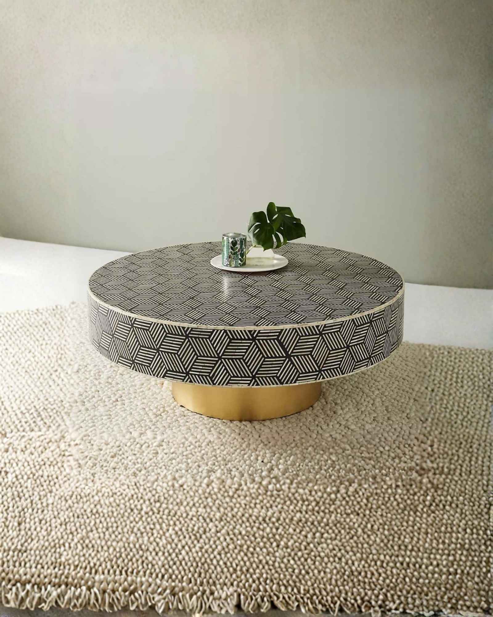 Round black bone inlay coffee table with a bold geometric pattern and gold base. A modern centerpiece for elegant living spaces.