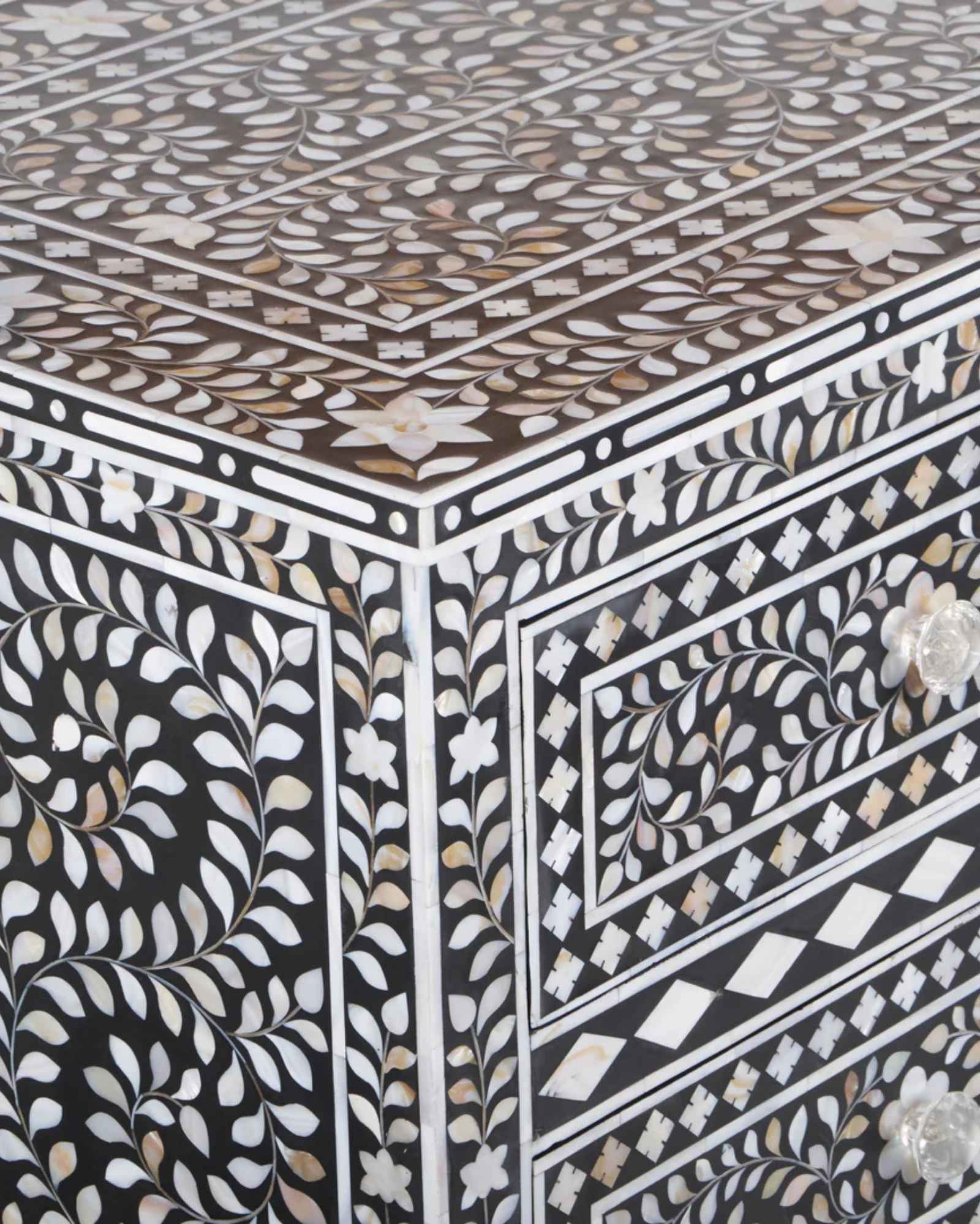 A handcrafted black mother of pearl inlay chest of drawers, featuring intricate floral patterns and geometric designs, with crystal knobs and smooth drawer slides.