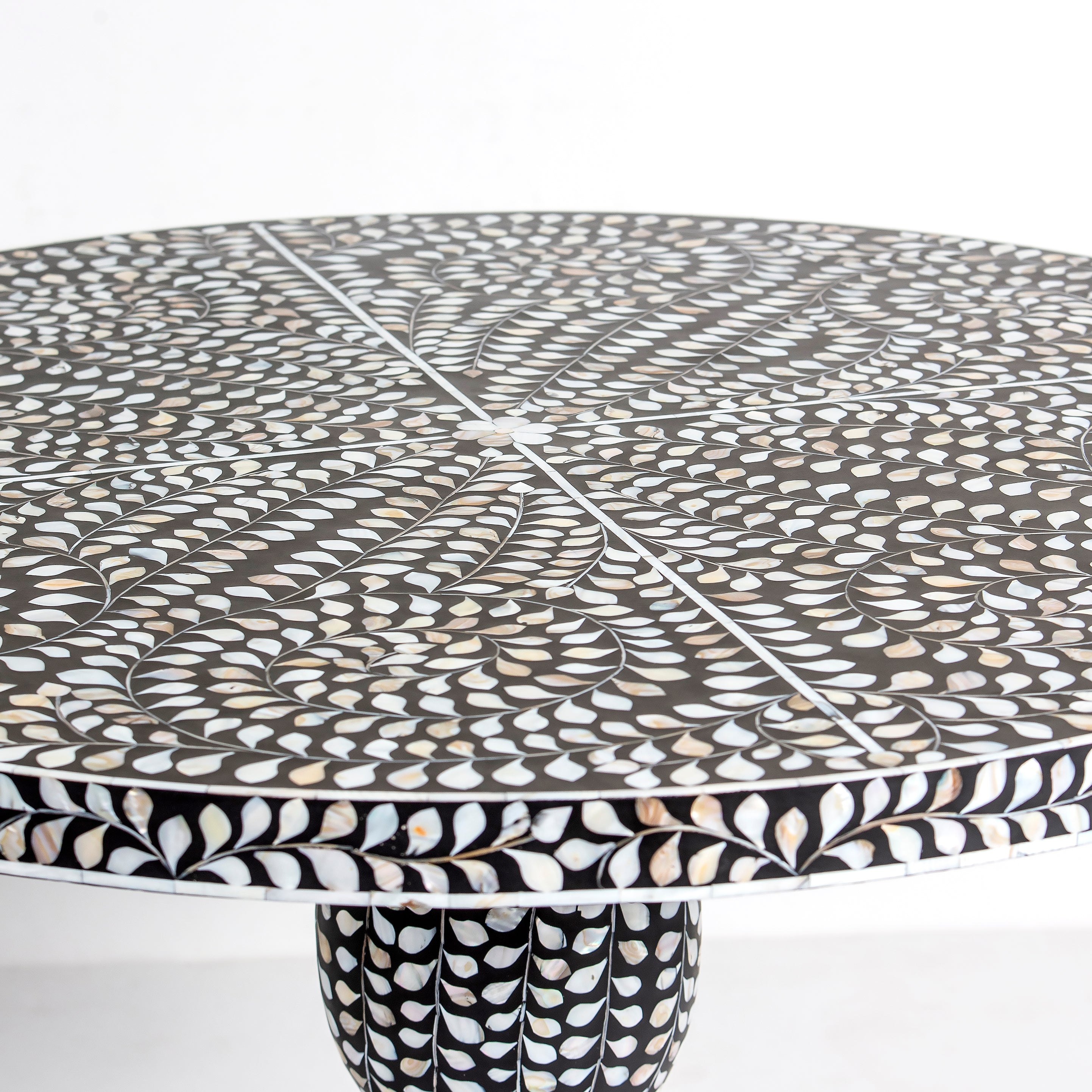 Handcrafted Iris dining table featuring black mother of pearl inlay with a round top and sculptural pedestal base.