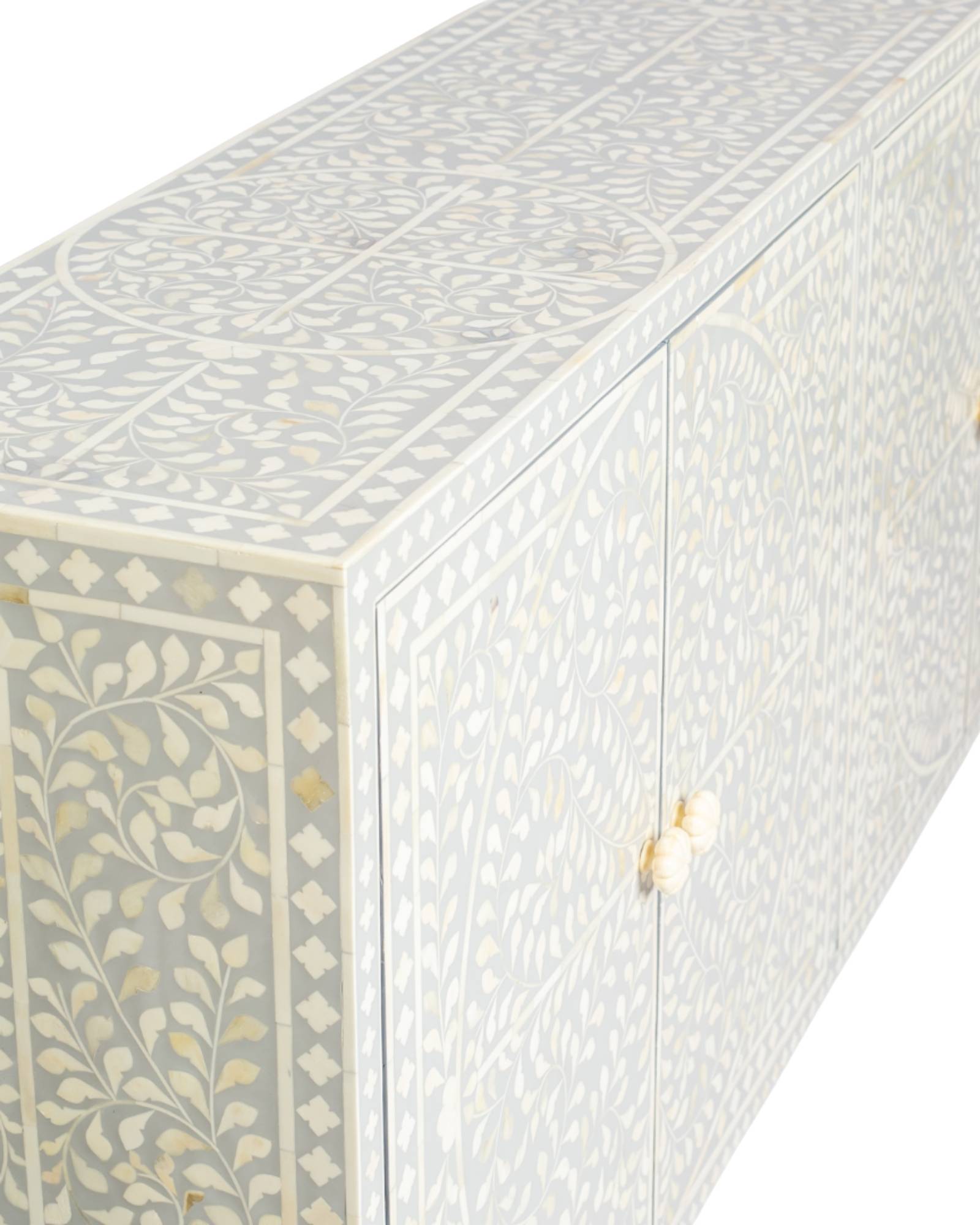 Grey bone inlay cabinet with floral vine pattern, brass legs, and carved bone knobs, handcrafted with spacious storage and artisanal charm.