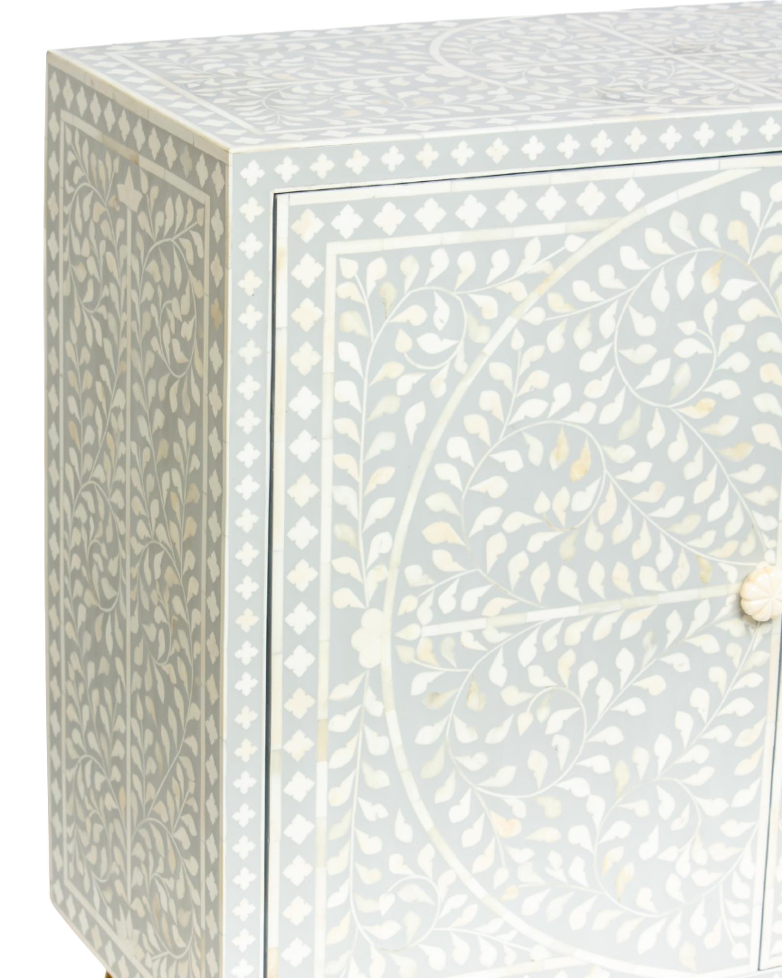 Grey bone inlay cabinet with floral vine pattern, brass legs, and carved bone knobs, handcrafted with spacious storage and artisanal charm.