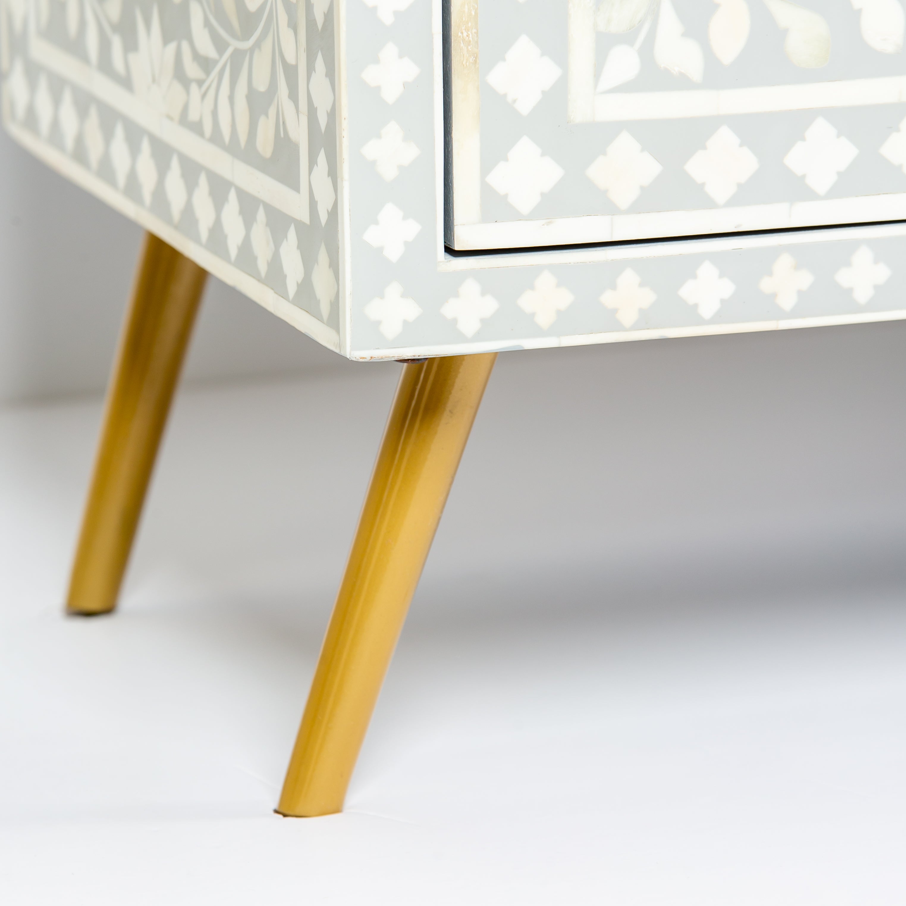 Grey bone inlay cabinet with floral vine pattern, brass legs, and carved bone knobs, handcrafted with spacious storage and artisanal charm.
