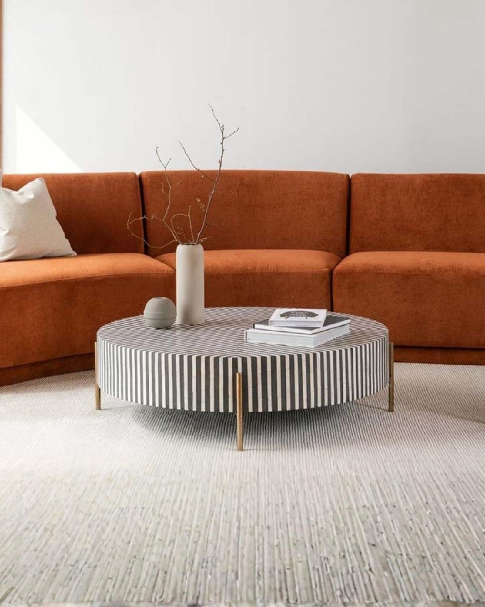 Round black bone inlay coffee table with striped design and brass legs.