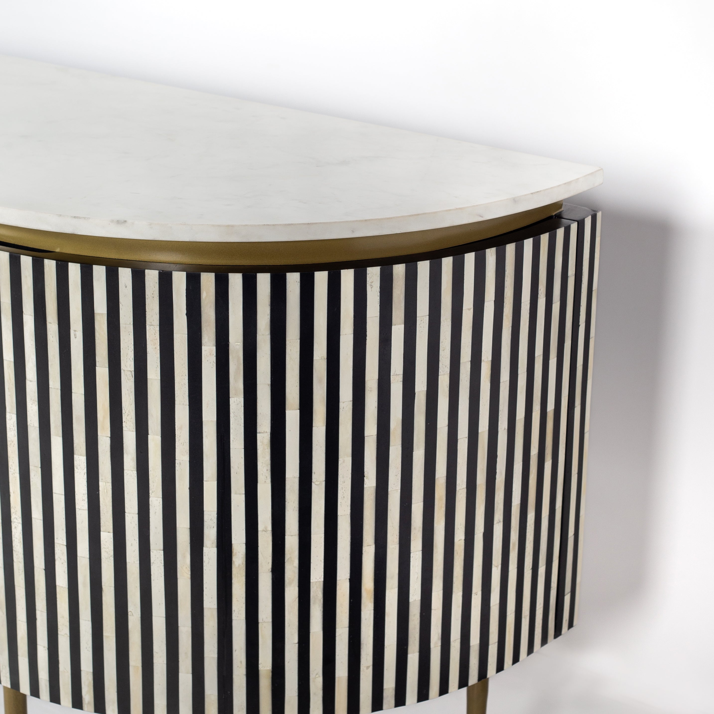 Black bone inlay sideboard with white marble top and brass legs, handcrafted with vertical striping and curved silhouette, luxury interior furniture.
