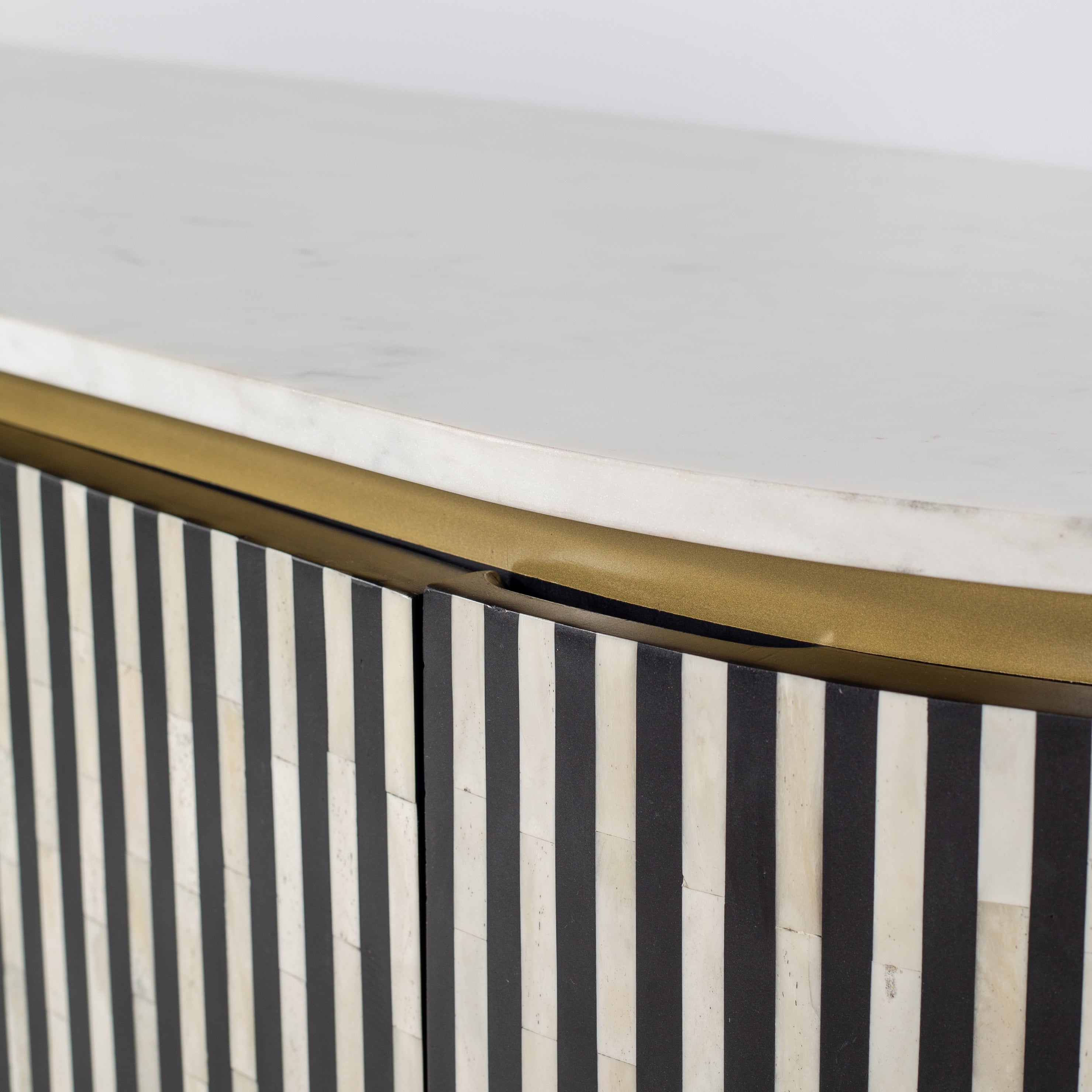 Black bone inlay sideboard with white marble top and brass legs, handcrafted with vertical striping and curved silhouette, luxury interior furniture.
