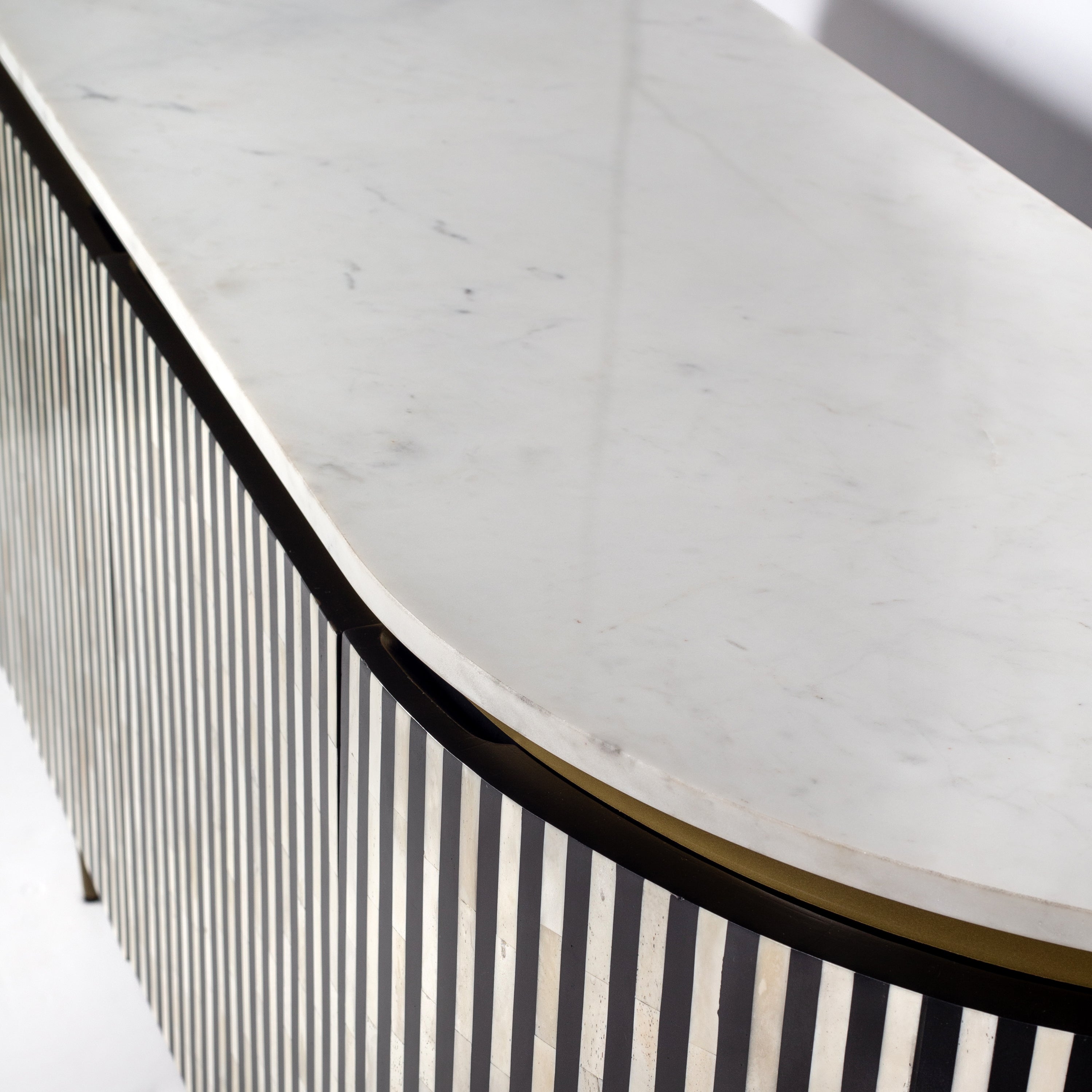Black bone inlay sideboard with white marble top and brass legs, handcrafted with vertical striping and curved silhouette, luxury interior furniture.
