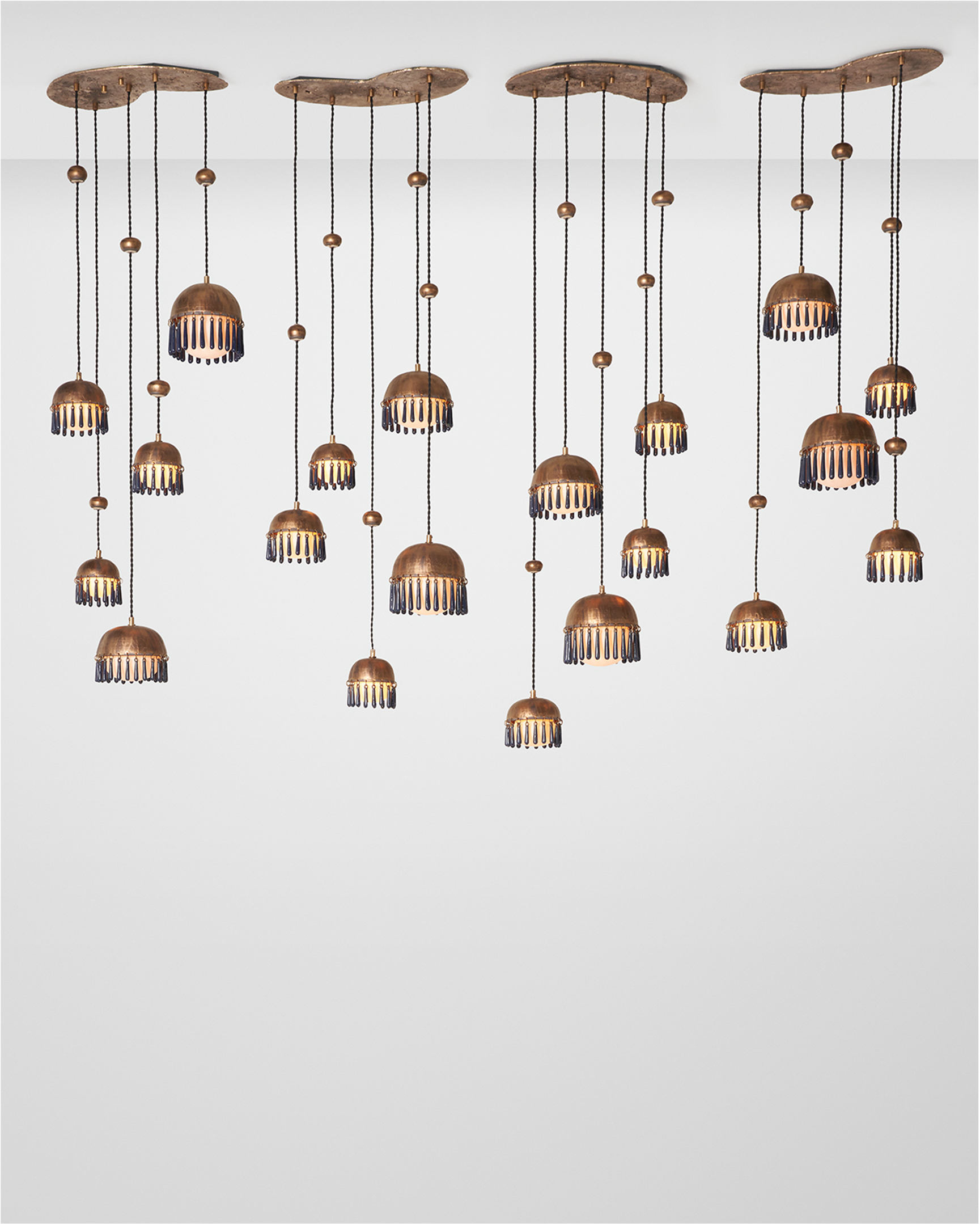 The Chime Chandelier by The Qratist features polished brass dome pendants with handcrafted porcelain drops suspended in a cascading cluster arrangement, creating an elegant sculptural lighting statement.